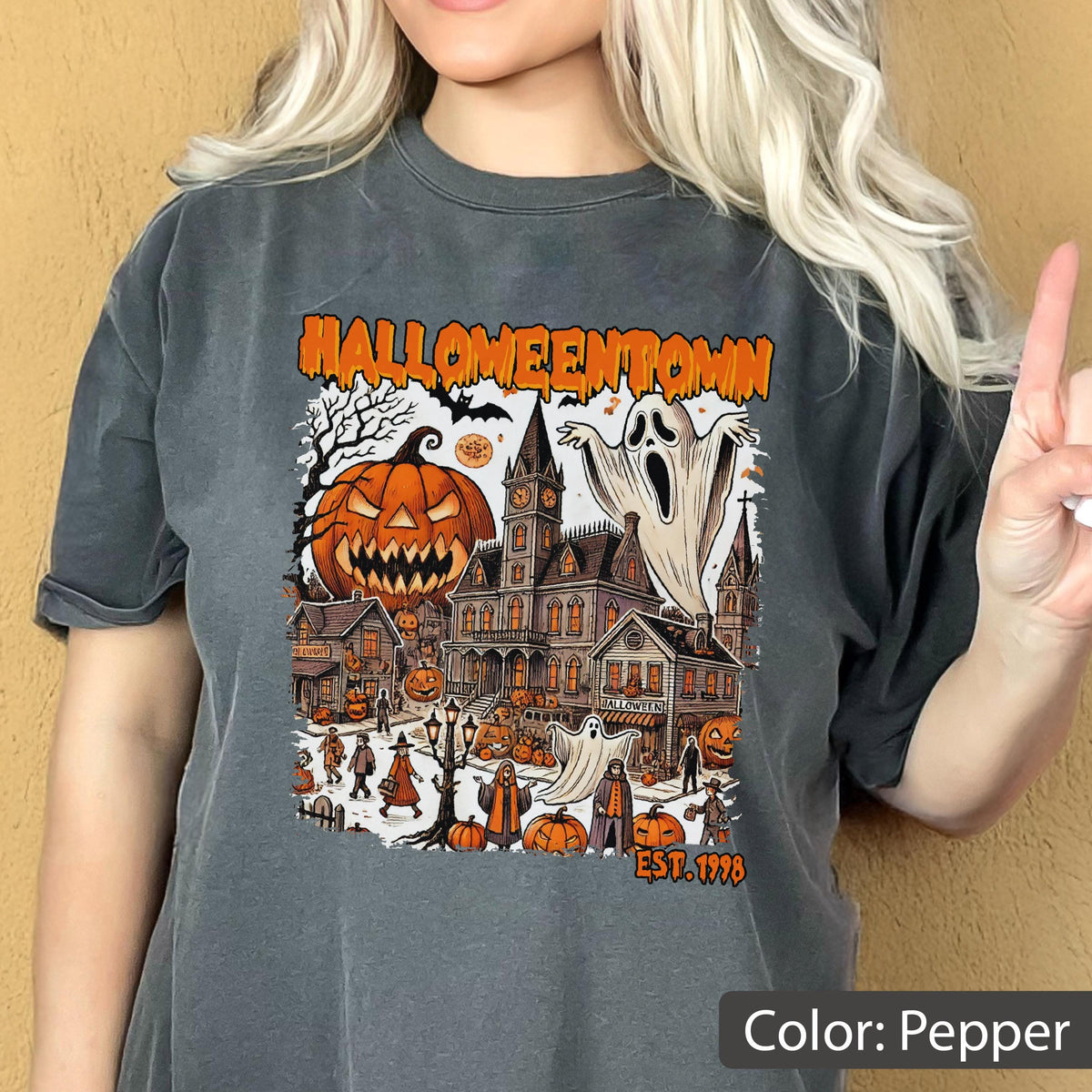 May include: A charcoal gray t-shirt featuring a graphic print with the text HALLOWEENTOWN and EST. 1998. The design includes a large jack-o'-lantern, a spooky mansion, ghosts, and various small figures in a town setting with orange and black accents.