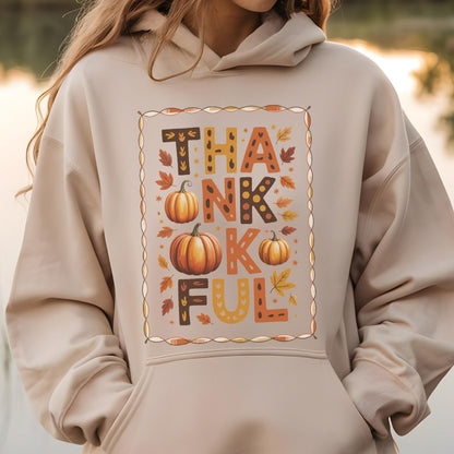 May include: Beige hoodie with the word "THANKFUL" in orange, brown, and yellow letters. The design includes three pumpkins and autumn leaves. The hoodie has a drawstring hood and a front pocket.