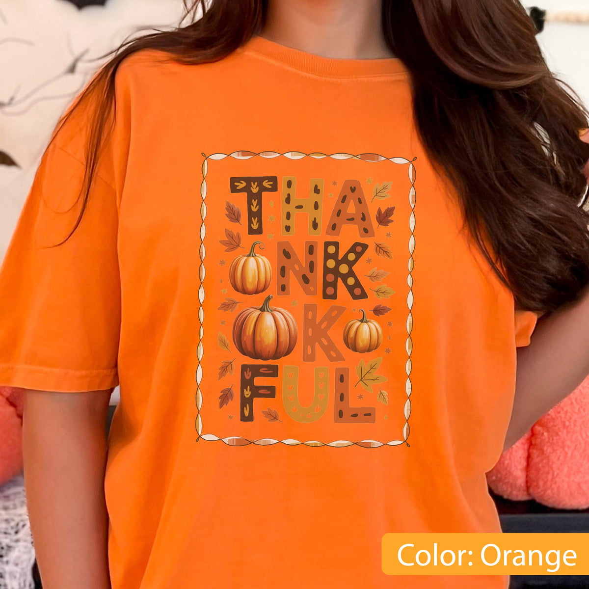 May include: Orange t-shirt with the word "THANKFUL" in a decorative frame. The design includes pumpkins and fall leaves. The shirt is a solid orange color, perfect for autumn.