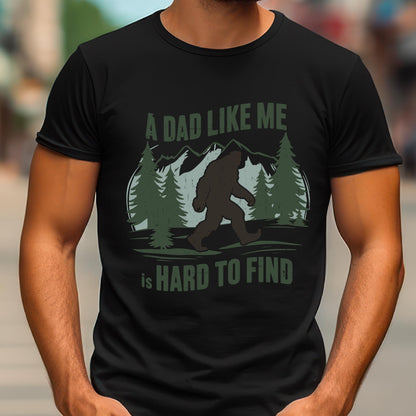 May include: A black short-sleeved t-shirt featuring a graphic print of a brown Bigfoot silhouette walking through a forest with mountains in the background. The text reads A DAD LIKE ME is HARD TO FIND in green and white lettering on the front.