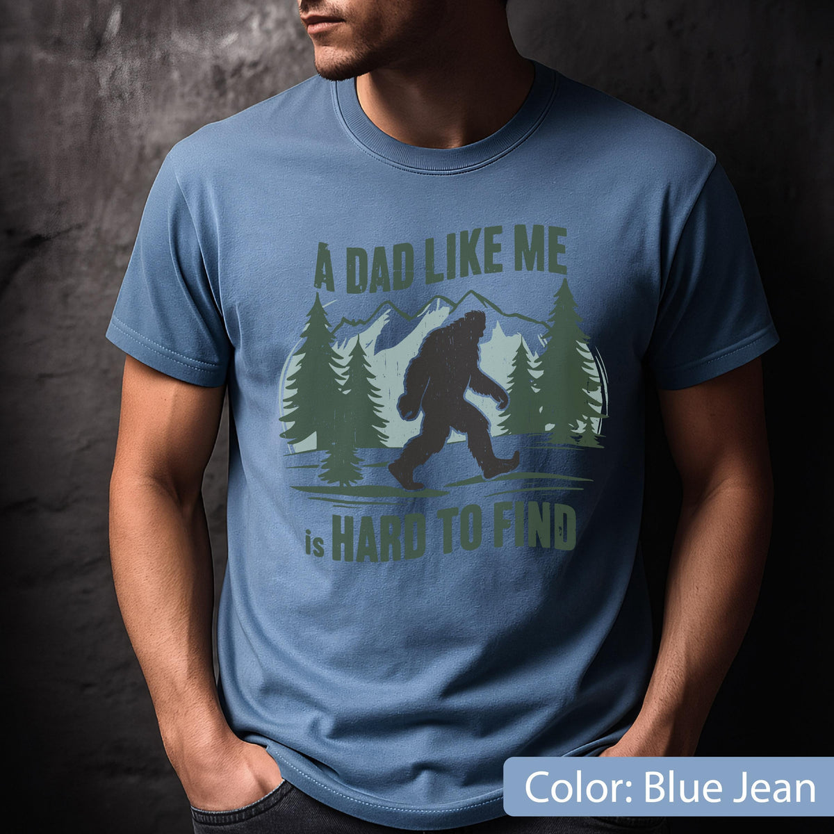 May include: Blue jean-colored t-shirt with a Bigfoot graphic and the text "A DAD LIKE ME is HARD TO FIND." The design features a silhouette of Bigfoot walking in front of a mountain and pine tree scene.