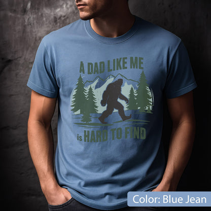 May include: Blue jean-colored t-shirt with a Bigfoot graphic and the text "A DAD LIKE ME is HARD TO FIND." The design features a silhouette of Bigfoot walking in front of a mountain and pine tree scene.