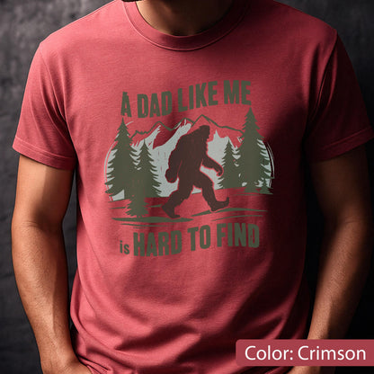 May include: Crimson t-shirt featuring a Bigfoot graphic walking in front of a mountain and trees. The text reads "A Dad Like Me is Hard to Find". The design is in shades of green and brown.