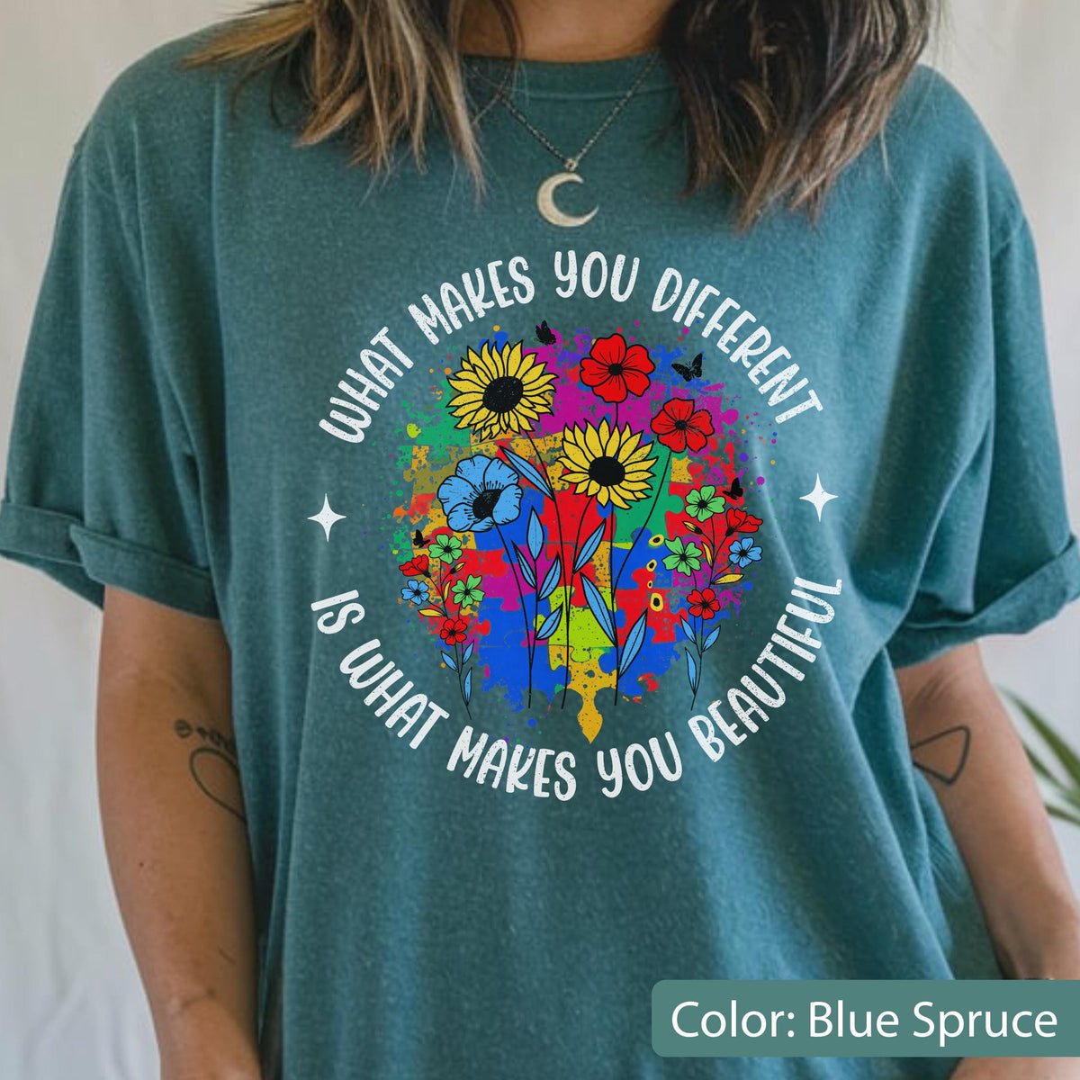 May include: Blue spruce t-shirt with a colorful floral design. The graphic includes sunflowers, red flowers, and blue flowers, with the text "WHAT MAKES YOU DIFFERENT IS WHAT MAKES YOU BEAUTIFUL" in a circular arrangement.