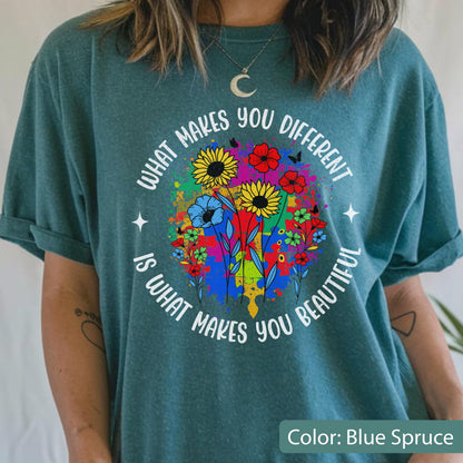 May include: Blue spruce t-shirt with a colorful floral design. The graphic includes sunflowers, red flowers, and blue flowers, with the text "WHAT MAKES YOU DIFFERENT IS WHAT MAKES YOU BEAUTIFUL" in a circular arrangement.