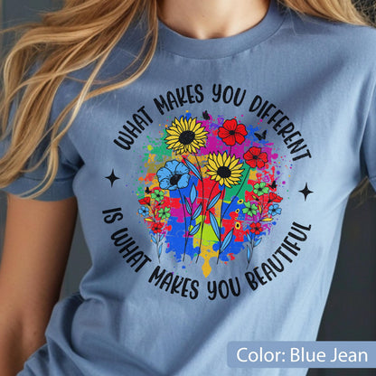 May include: Blue jean-colored t-shirt featuring a colorful floral design with the text "WHAT MAKES YOU DIFFERENT IS WHAT MAKES YOU BEAUTIFUL." The design includes sunflowers, red flowers, and blue flowers, with a splash of colorful paint.