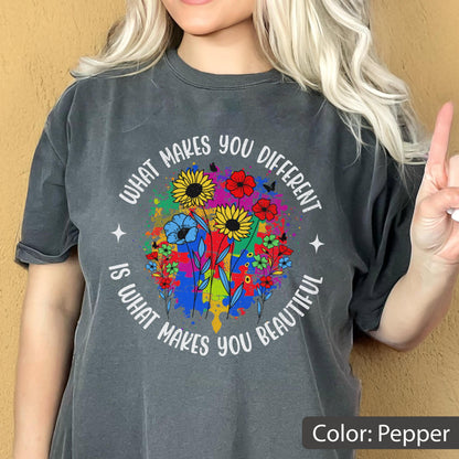 May include: Pepper-colored t-shirt with a colorful floral design. The design features sunflowers, red and blue flowers, and butterflies, with the text "WHAT MAKES YOU DIFFERENT IS WHAT MAKES YOU BEAUTIFUL" in a circular arrangement.