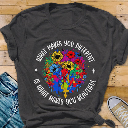 May include: Dark gray t-shirt featuring a colorful floral design with the text "WHAT MAKES YOU DIFFERENT IS WHAT MAKES YOU BEAUTIFUL" in a circular pattern. The design includes sunflowers, butterflies, and a puzzle piece.