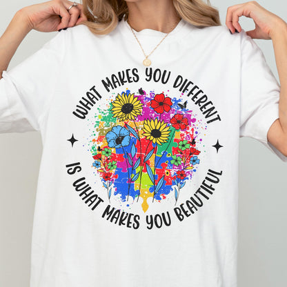 May include: White t-shirt with the text "WHAT MAKES YOU DIFFERENT IS WHAT MAKES YOU BEAUTIFUL" in a circular design. The design features colorful flowers and puzzle pieces, with a splash of paint.