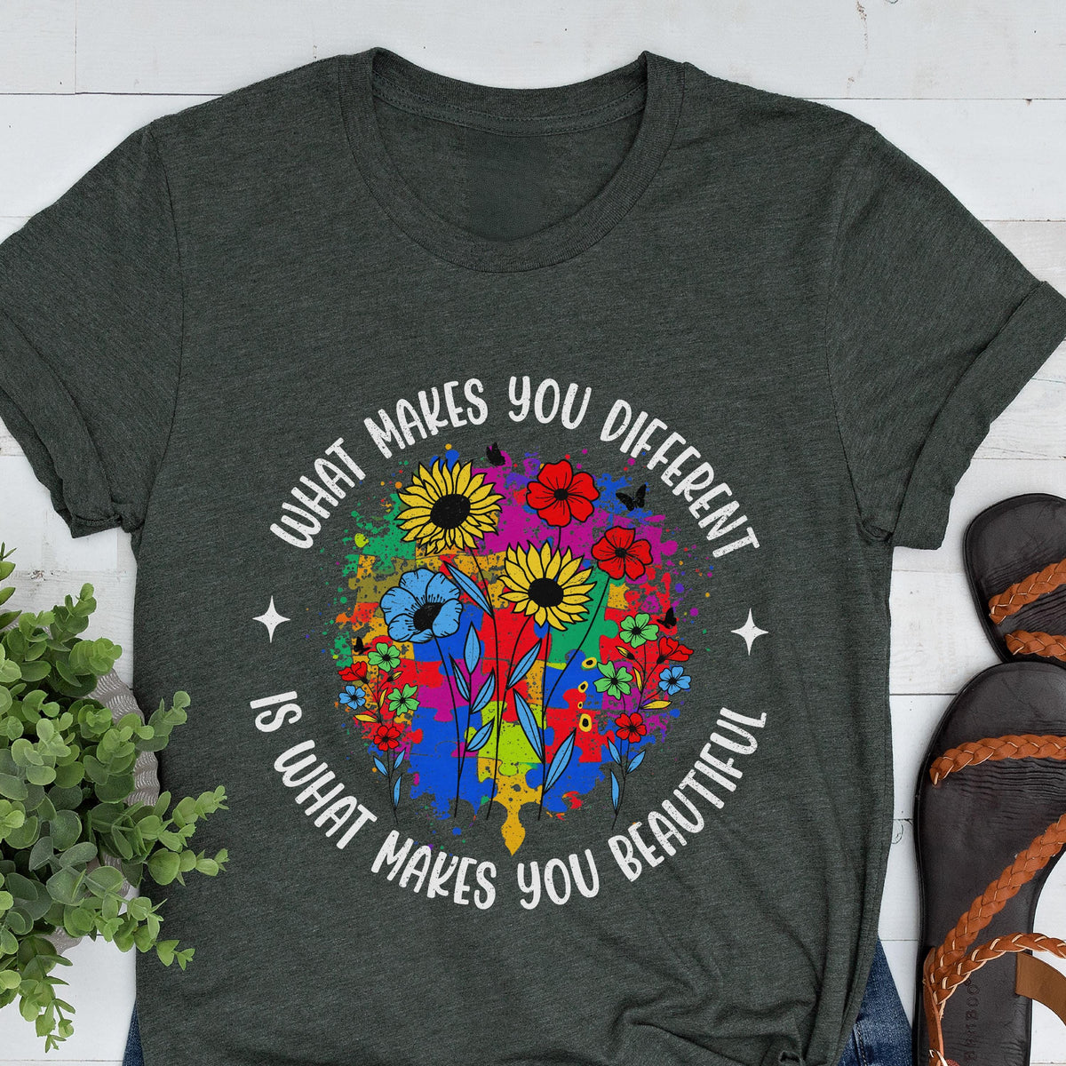 May include: Dark gray t-shirt with a colorful floral design. The design includes sunflowers, red flowers, and blue flowers, with the text "What makes you different is what makes you beautiful" in a circular pattern.