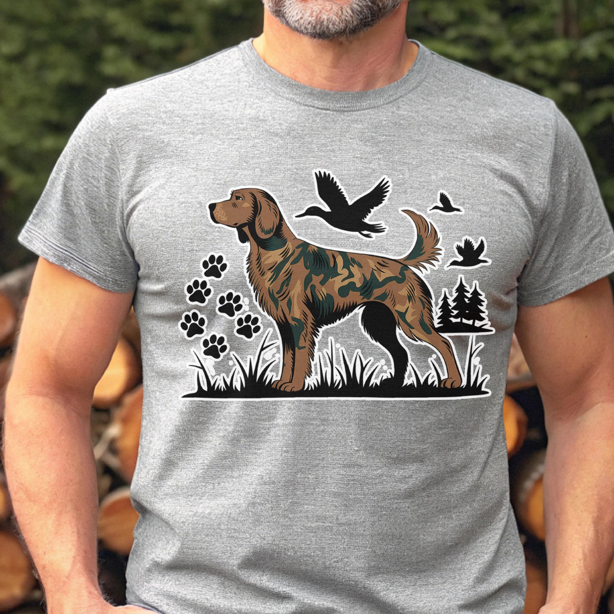 May include: A heather gray short-sleeve t-shirt featuring a graphic print of a brown dog with a camouflage pattern on its body. The design includes black silhouettes of flying ducks, paw prints, and pine trees set against a grassy landscape.