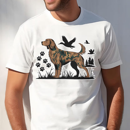 May include: A white short-sleeved t-shirt featuring a graphic print of a brown dog with a camouflage pattern. The design includes black silhouettes of flying ducks, pine trees, and several paw prints set against a patch of black grass.