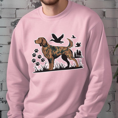 May include: A light pink sweatshirt featuring a brown and green dog illustration with paw prints, trees, and flying birds. The dog has a camouflage pattern. The sweatshirt is made of a soft material.