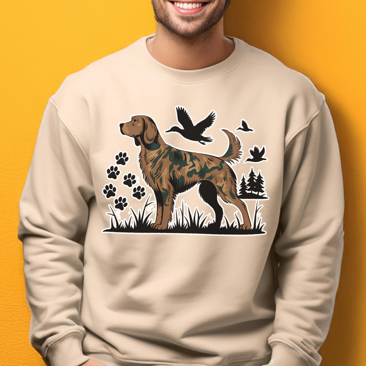May include: Beige sweatshirt featuring a dog illustration with a camouflage pattern. The design includes black paw prints, birds, and trees. The dog is standing in grass. The sweatshirt is a neutral color.