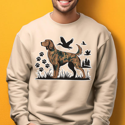 May include: Beige sweatshirt featuring a dog illustration with a camouflage pattern. The design includes black paw prints, birds, and trees. The dog is standing in grass. The sweatshirt is a neutral color.