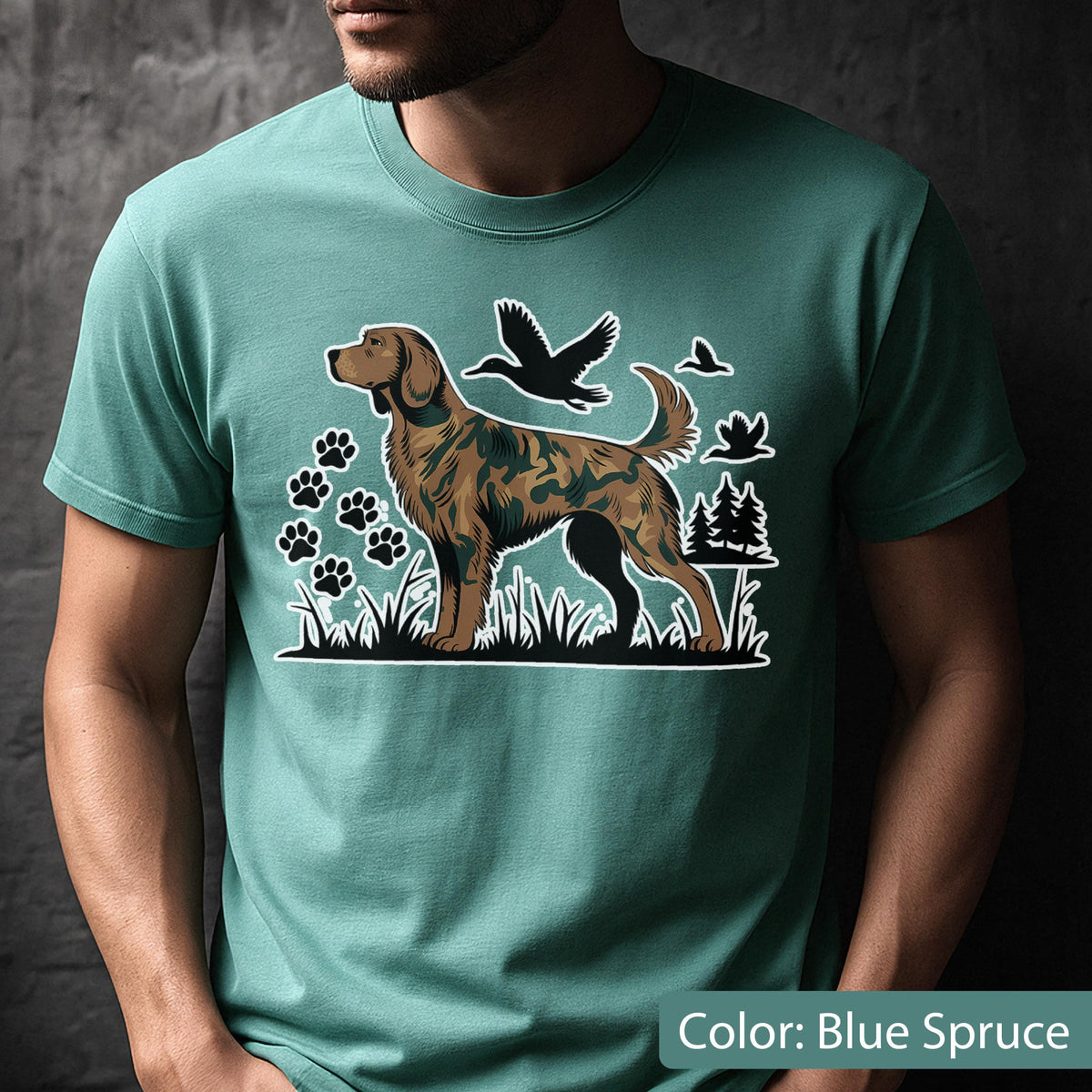 May include: A blue spruce crew neck t-shirt featuring a graphic print of a hunting dog with a camouflage pattern. The design includes black silhouettes of flying ducks, paw prints, and pine trees set against a grassy landscape background.