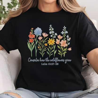 May include: Black t-shirt featuring a colorful floral design with the text "Consider how the wildflowers grow" and the Bible verse Luke 12:27-28. The flowers include orange, blue, pink, yellow, and peach blooms.