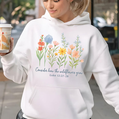 May include: White hoodie with a floral design featuring colorful wildflowers in shades of red, blue, yellow, and peach. The text "Consider how the wildflowers grow" and Luke 12:27-28 are printed in blue script. The hoodie has a front pocket.