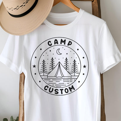 May include: A white short-sleeved t-shirt featuring a black circular graphic on the chest. The design includes a tent, pine trees, a crescent moon, and stars, with the text CAMP CUSTOM printed in a bold, sans-serif font within the circular border.