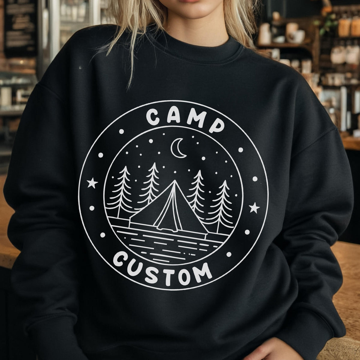 May include: A black crewneck sweatshirt featuring a white circular graphic on the chest. The design depicts a tent, pine trees, a crescent moon, and stars above a body of water, with the text CAMP CUSTOM printed along the circular border.