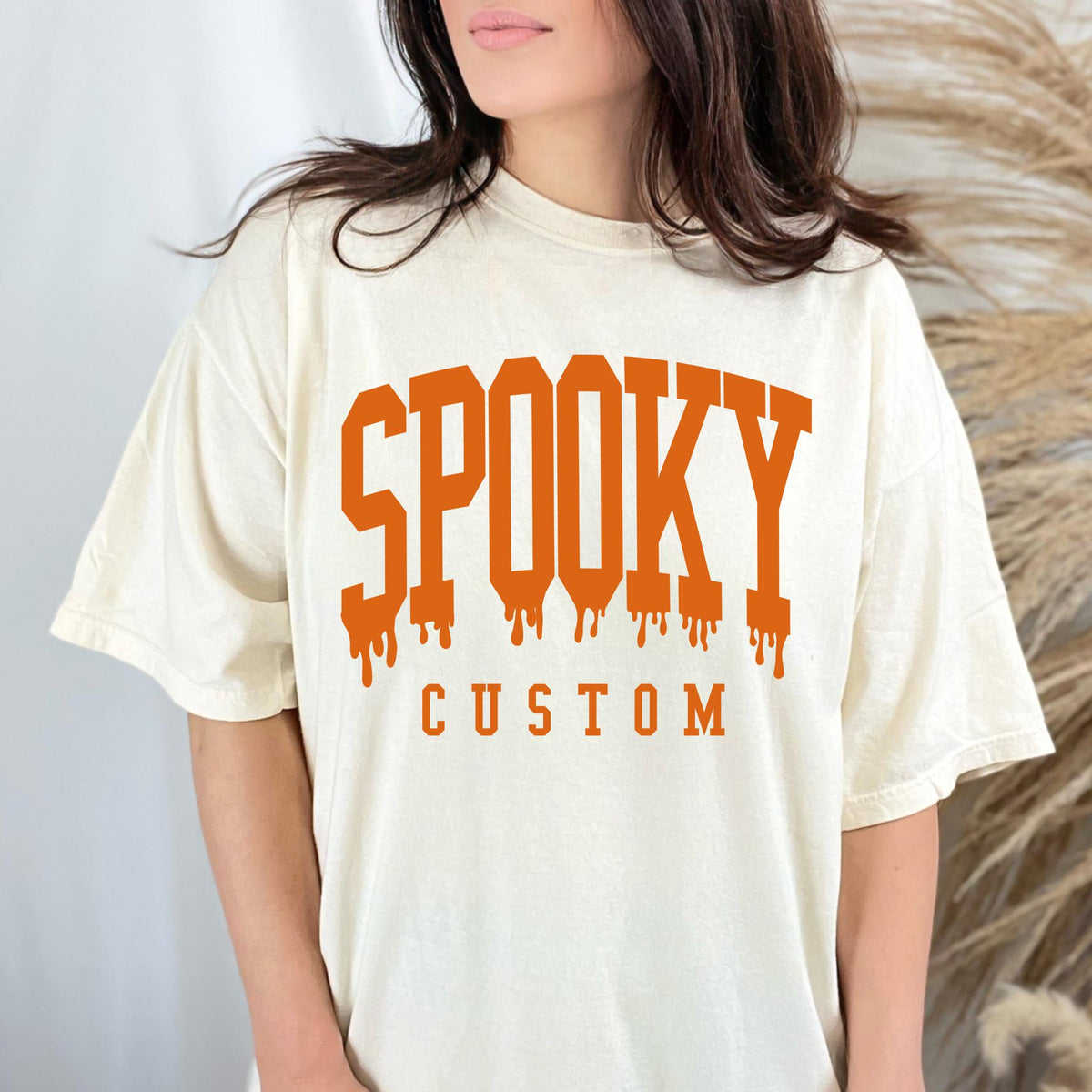 May include: Cream-colored t-shirt with the word "SPOOKY" in orange block letters with dripping effect, and the word "CUSTOM" below. The shirt has a relaxed fit.