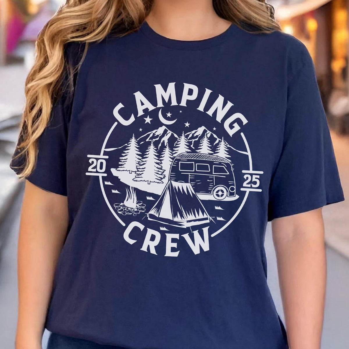 May include: A navy blue short-sleeve t-shirt featuring a white circular graphic with the text "CAMPING CREW" and "20 25". The design includes a camper van, a tent, a campfire, pine trees, mountains, and a crescent moon with stars.