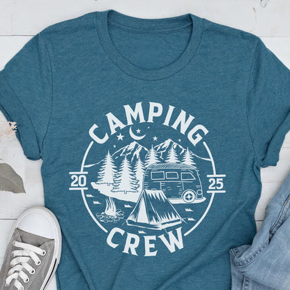 May include: A teal blue short-sleeve t-shirt featuring a white circular graphic print. The design includes a camper van, a tent, a campfire, pine trees, mountains, stars, and a crescent moon, with the text "CAMPING CREW" and "2025".