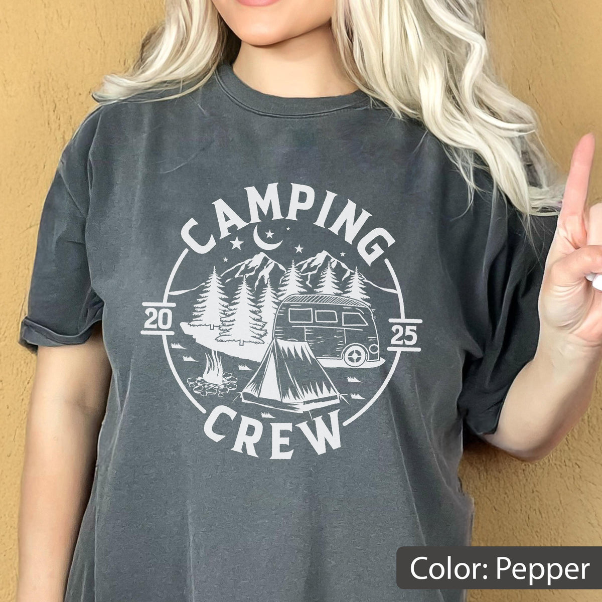 May include: A charcoal gray short-sleeve t-shirt featuring a white circular graphic with the text "CAMPING CREW" and "2025". The design includes a camper van, a tent, pine trees, mountains, a crescent moon, and stars, all printed on the front.