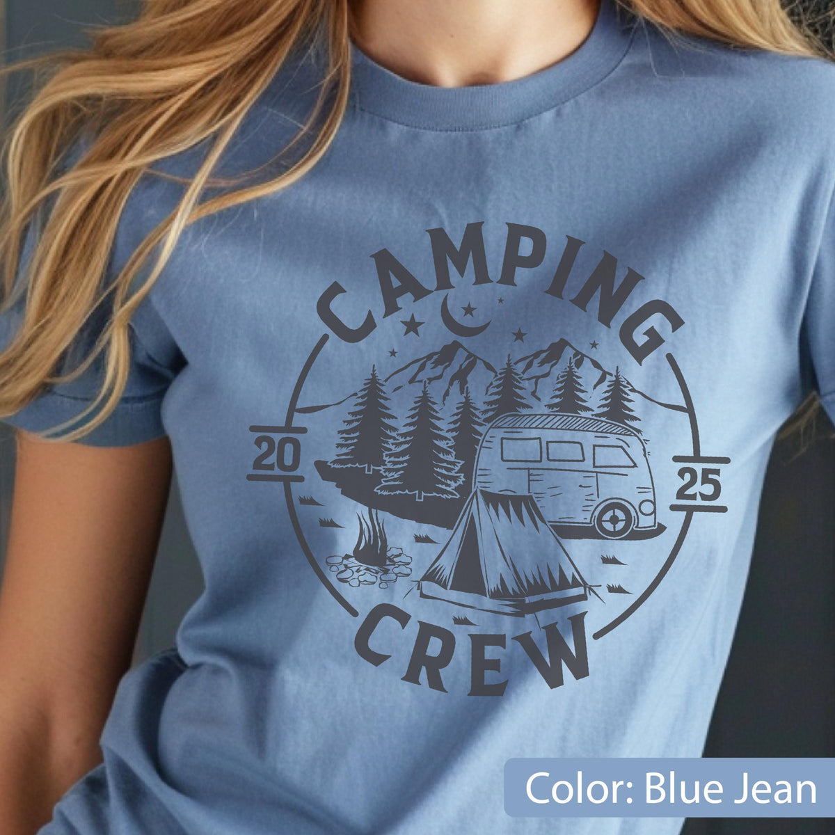 May include: A blue jean colored t-shirt featuring a dark gray circular graphic. The design includes the text CAMPING CREW, the numbers 20 and 25, a mountain range, pine trees, a crescent moon, stars, a camper van, and a tent with a campfire.