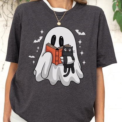 May include: A dark heather gray t-shirt featuring a graphic of a white ghost reading an orange book while holding a small black cat. The design includes white stars and small bat silhouettes surrounding the ghost, set against a dark fabric background.