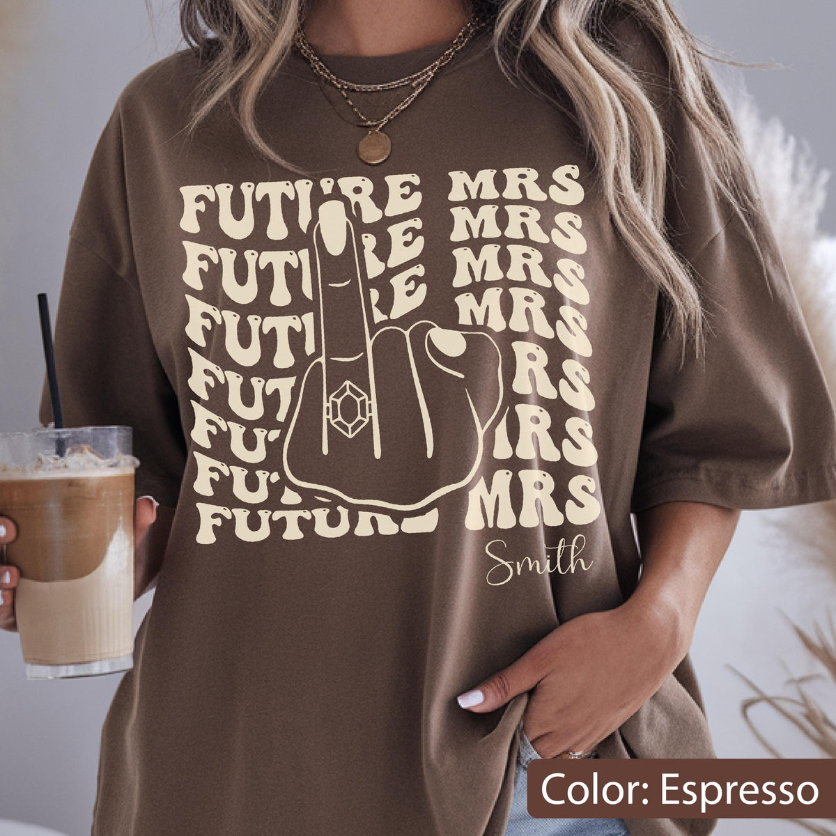 May include: An espresso brown t-shirt featuring a cream-colored graphic of a hand with a ring on the middle finger. The text "FUTURE" is repeated on the left and "MRS" on the right, with the name "Smith" printed in a script font below.