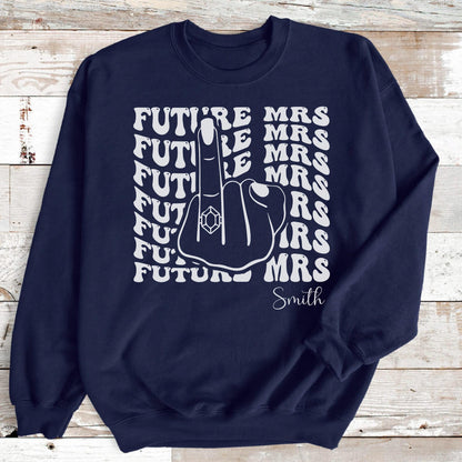 May include: Navy blue sweatshirt with a white graphic. The graphic features the words "FUTURE MRS" in a wavy font, along with a hand giving the middle finger, a ring on the finger, and the last name "Smith".