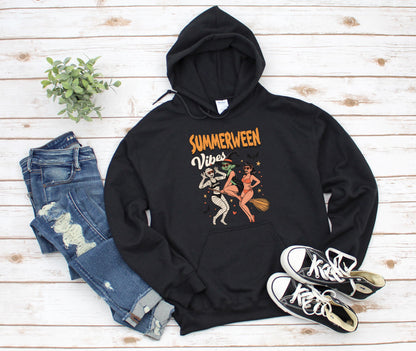 May include: Black hooded sweatshirt with the text "Summerween Vibes" and a graphic of three cartoon figures. The figures include a mummy, a witch, and a woman riding a broom. The sweatshirt is paired with blue jeans and black sneakers.