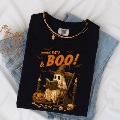 May include: Black t-shirt with a Halloween-themed graphic. The design features a ghost reading a book in a rocking chair, surrounded by bats, candles, a pumpkin, and the text "BOOKS BATS & BOO!". A gold necklace is draped over the shirt.