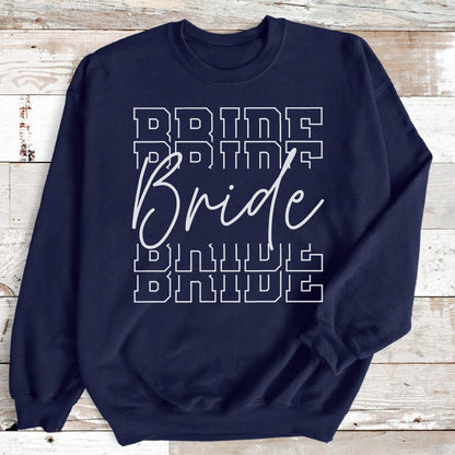 May include: A navy blue crewneck sweatshirt featuring the word Bride printed in a white script font, layered over and under the word BRIDE repeated four times in a white block varsity-style font with a thin outline, centered on the chest.