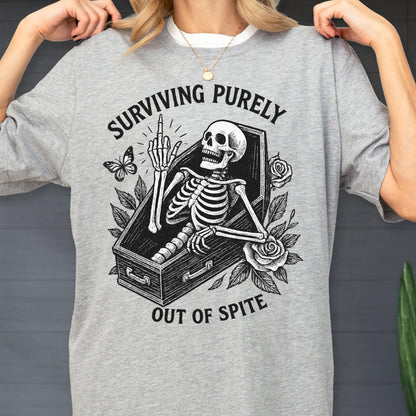 May include: A heather gray t-shirt featuring a black graphic of a skeleton inside a coffin, giving the middle finger. The design includes roses, a butterfly, and the text "SURVIVING PURELY OUT OF SPITE" arched around the central illustration.