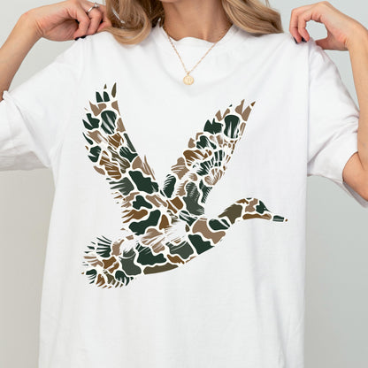 May include: A white short-sleeved t-shirt featuring a large graphic of a flying duck on the front. The duck silhouette is filled with a camouflage pattern consisting of dark green, brown, and tan organic shapes against the white fabric background.