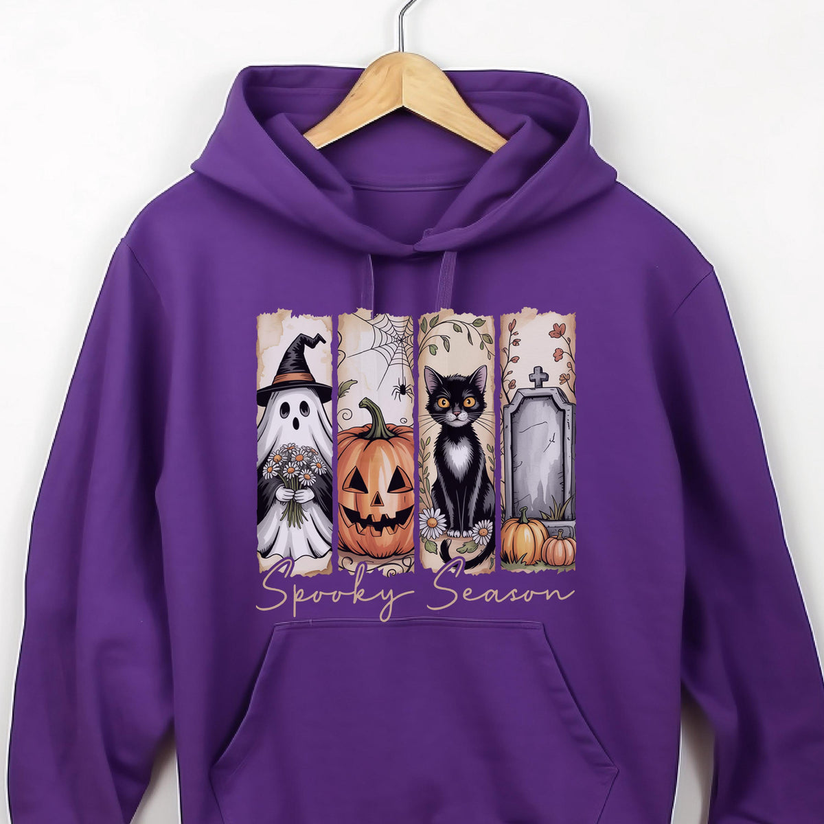 May include: A purple hooded sweatshirt featuring a graphic print divided into four vertical panels. The panels display a ghost in a witch hat, a jack-o'-lantern, a black cat, and a tombstone. The text "Spooky Season" is printed below the panels.