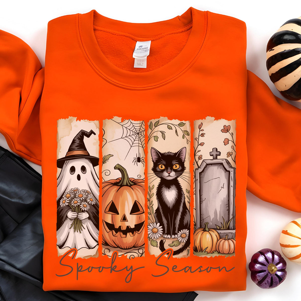 May include: An orange crewneck sweatshirt featuring a graphic print with four vertical panels depicting a ghost in a witch hat holding flowers, a jack-o'-lantern, a black cat, and a tombstone, with the text Spooky Season written below.