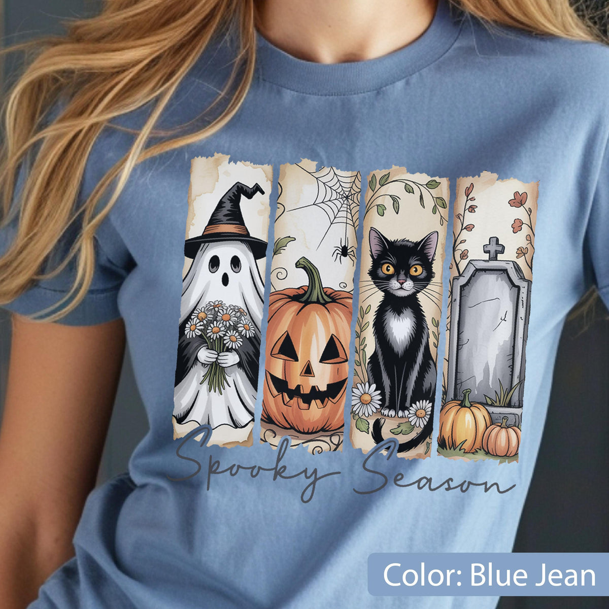 May include: Blue jean t-shirt featuring a Halloween-themed graphic. The design includes a ghost, jack-o'-lantern, black cat, and tombstone. The words "Spooky Season" are written in a script font. The shirt is a light blue color.