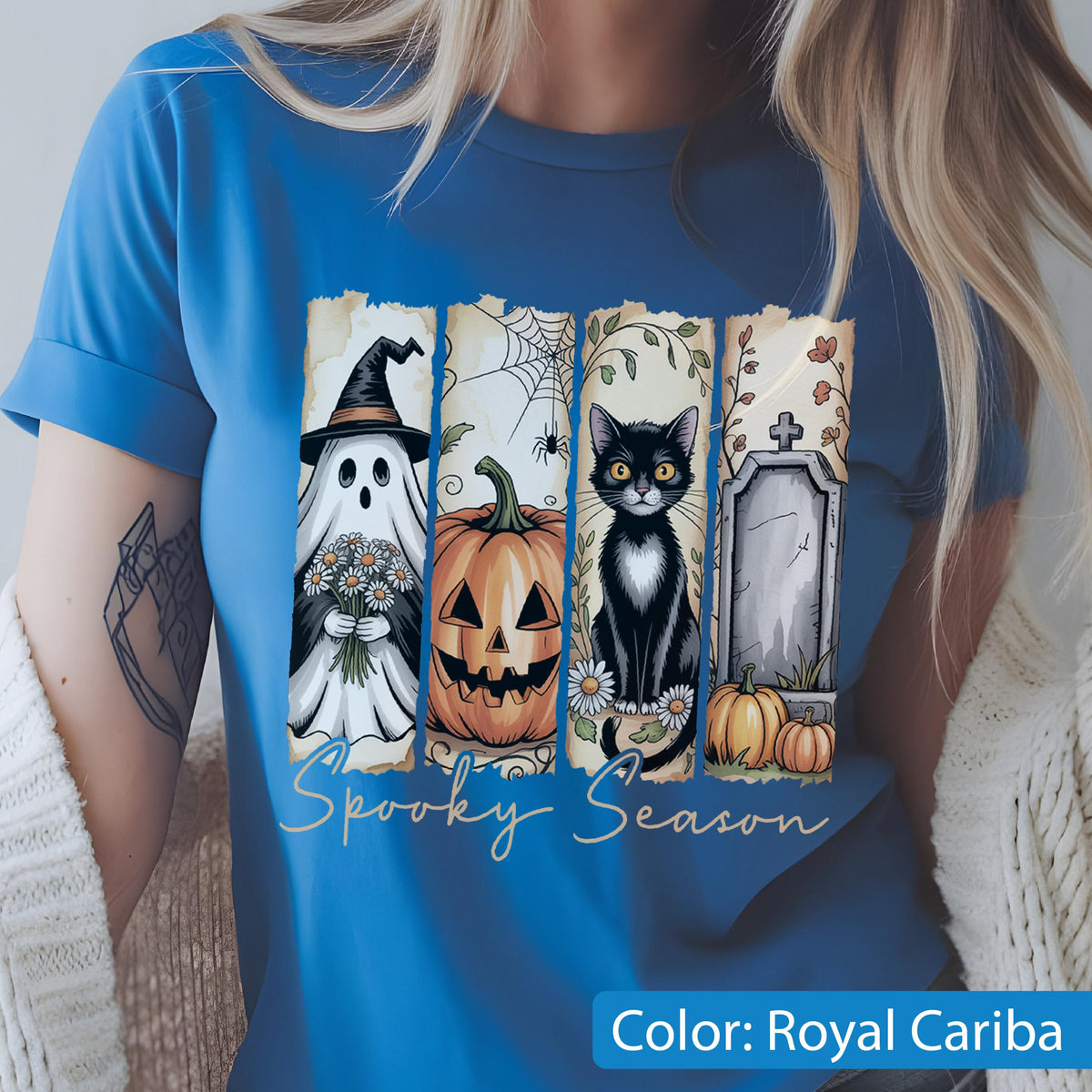 May include: Royal Cariba blue t-shirt featuring a Halloween-themed design. The design includes a ghost, jack-o'-lantern, black cat, and tombstone. The words "Spooky Season" are written in a script font.