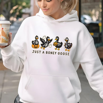 May include: White hooded sweatshirt featuring a Halloween-themed graphic. The design includes four cartoon geese dressed as skeletons, holding pumpkins, and accompanied by ghosts. The text "JUST A BONEY GOOSE" is printed below the geese.