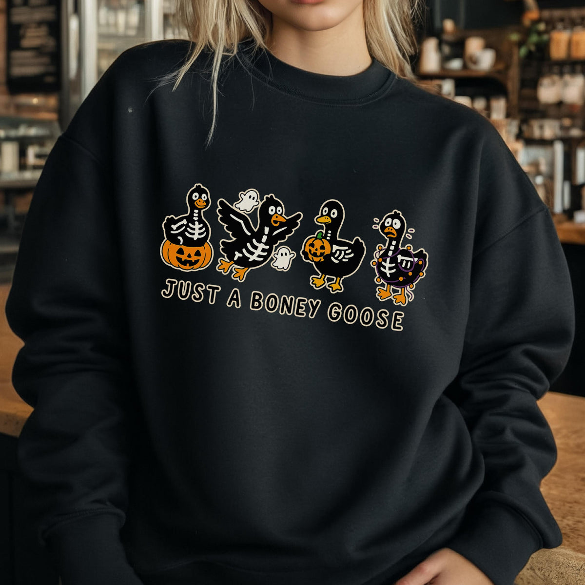 May include: Black sweatshirt with a Halloween-themed graphic. The design features four cartoon geese in skeleton costumes, holding pumpkins and accompanied by ghosts. The text "JUST A BONEY GOOSE" is below the geese.
