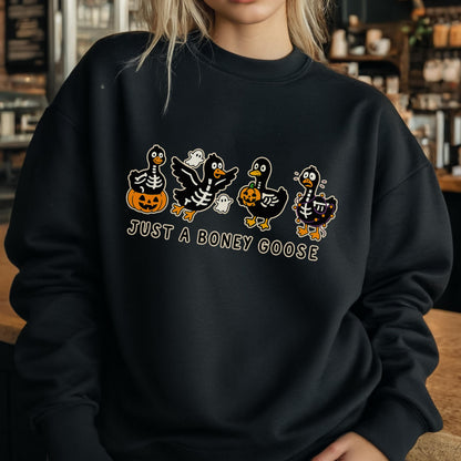 May include: Black sweatshirt with a Halloween-themed graphic. The design features four cartoon geese in skeleton costumes, holding pumpkins and accompanied by ghosts. The text "JUST A BONEY GOOSE" is below the geese.
