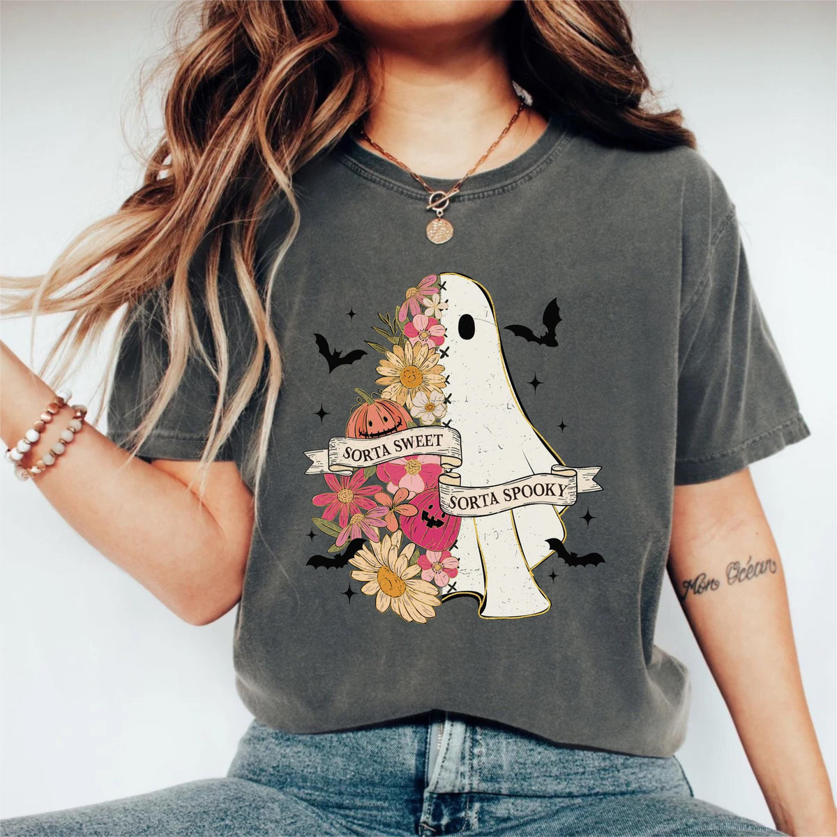 May include: Dark grey t-shirt featuring a ghost design with floral elements and bats. The ghost is half-filled with flowers and a pumpkin. Text on the shirt reads "Sorta Sweet" and "Sorta Spooky".