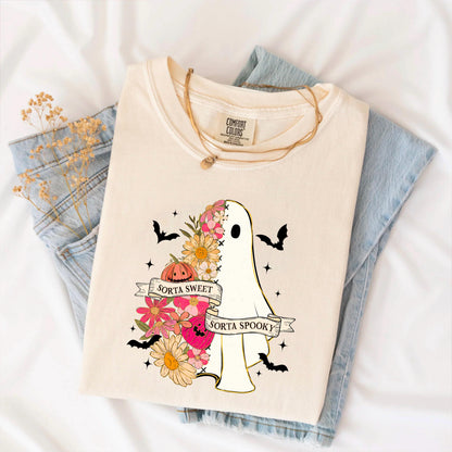 May include: Cream-colored t-shirt with a ghost graphic. The ghost is decorated with flowers and a pumpkin, and the text "Sorta Sweet Sorta Spooky" is displayed on a banner. Black bats and stars surround the ghost.