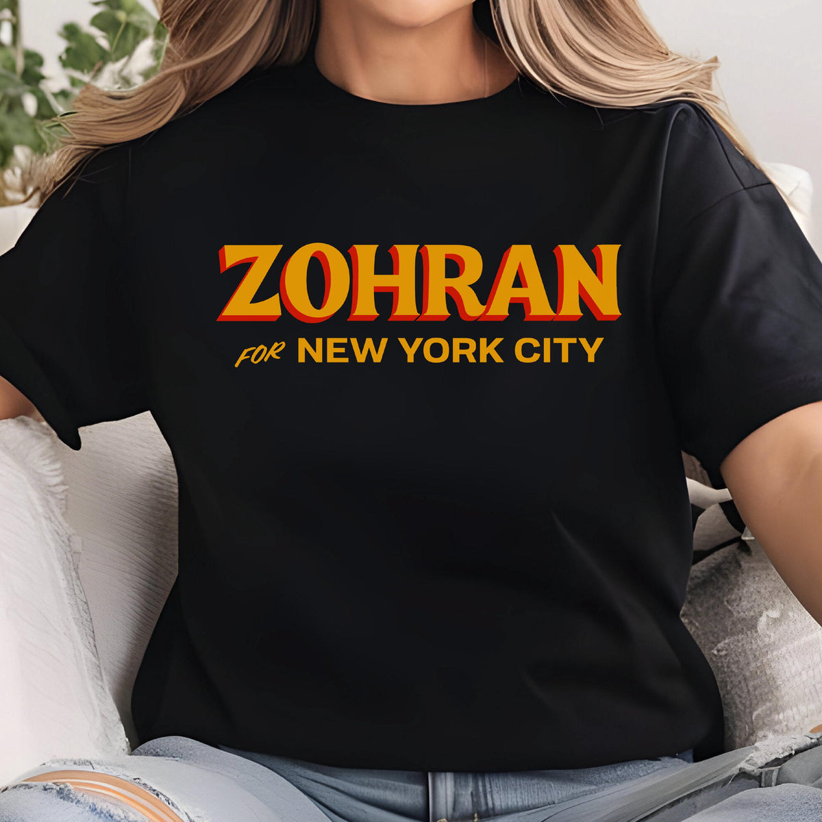 May include: A black short-sleeved t-shirt featuring the text ZOHRAN in large yellow letters with a red drop shadow, positioned above the text FOR NEW YORK CITY in smaller yellow letters. The shirt has a crew neckline and a standard fit.