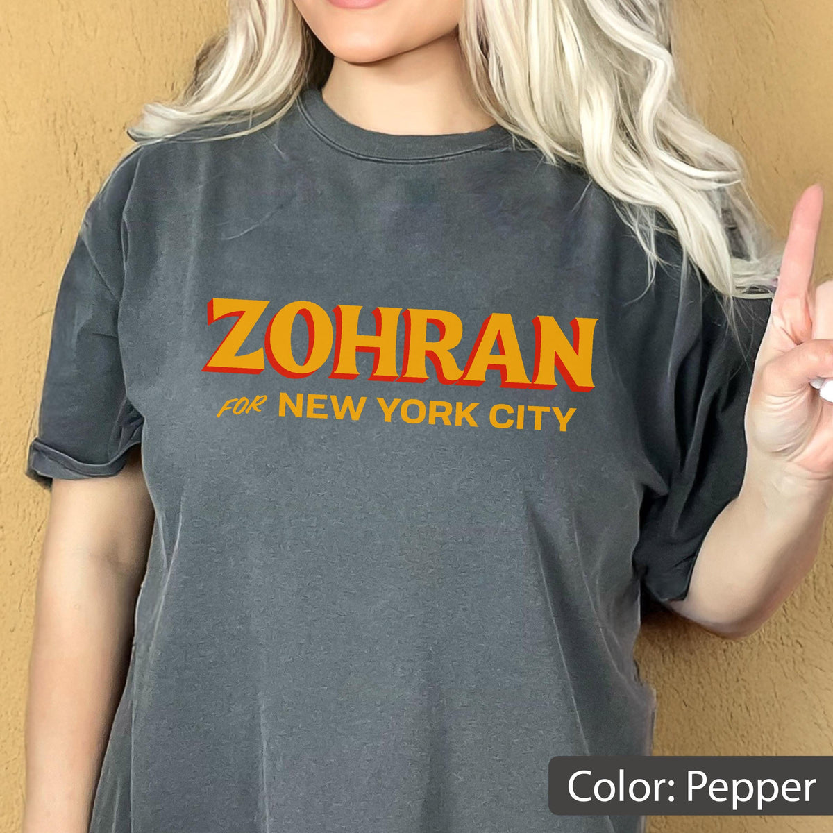 May include: Pepper-colored t-shirt with the text "ZOHRAN" in orange letters with a red outline, and "for NEW YORK CITY" in orange. The shirt is a dark gray color.