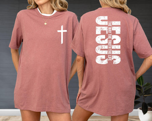 May include: A dusty rose-colored t-shirt with a white cross on the front and the word "JESUS" printed vertically on the back, along with the text "THE WAY THE TRUTH THE LIFE". The shirt has a crew neck and short sleeves.