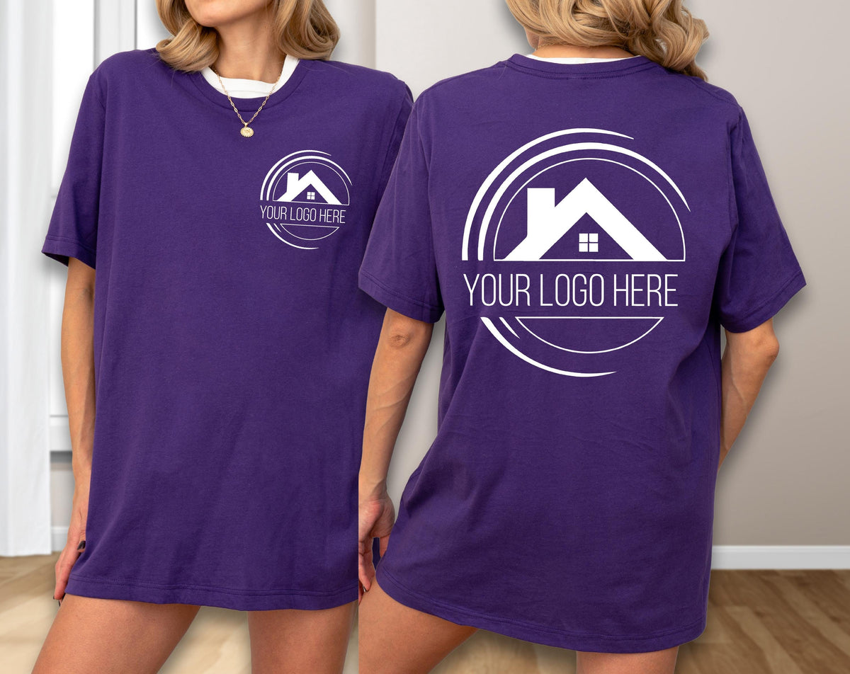 May include: A purple t-shirt with a white collar and a white logo on the front and back. The logo features a house silhouette inside a circular design, with the text "YOUR LOGO HERE" below. The shirt is a solid color.
